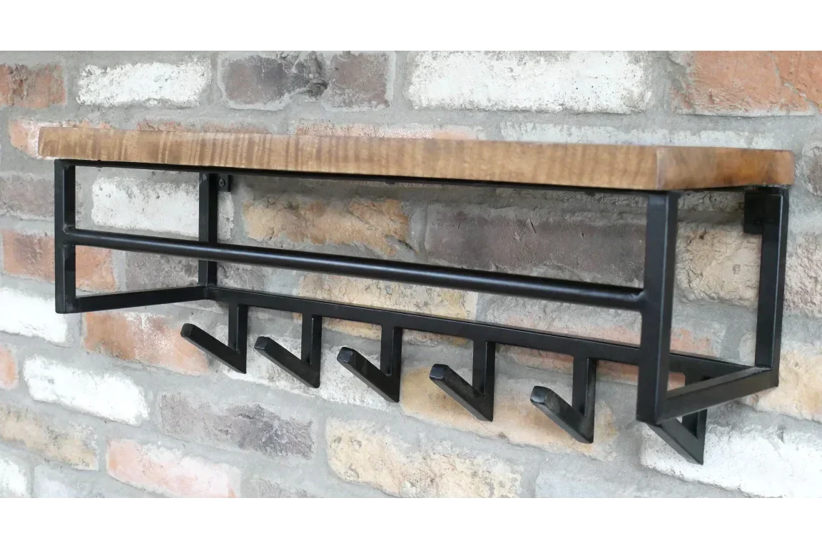 Wall mounted coat rack with black metal hooks and a wooden shelf on brick wall