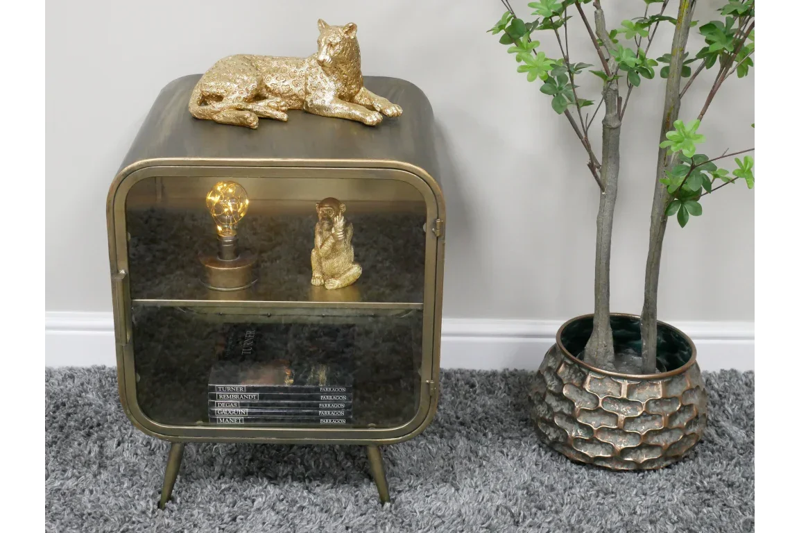 Brass and glass display cabinet with gold animal decor beside potted artificial tree on carpet