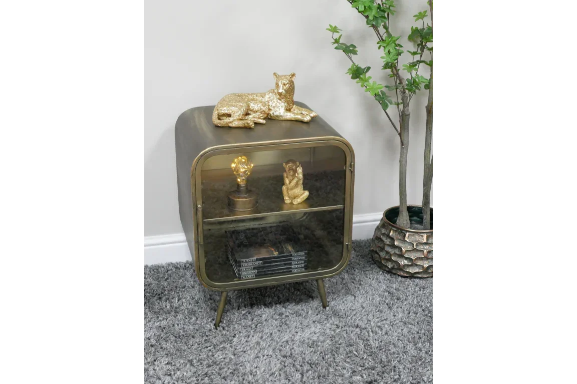 Metal side cabinet with glass door, gold ornaments, books, and decorative lamp on grey carpet