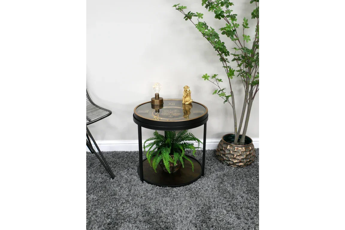 Round glass top side table with clock face, black metal legs, and shelf holding a fern plant