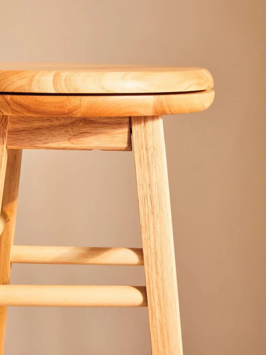 Closeup of light wood stool showing seat edge, leg, and horizontal rungs