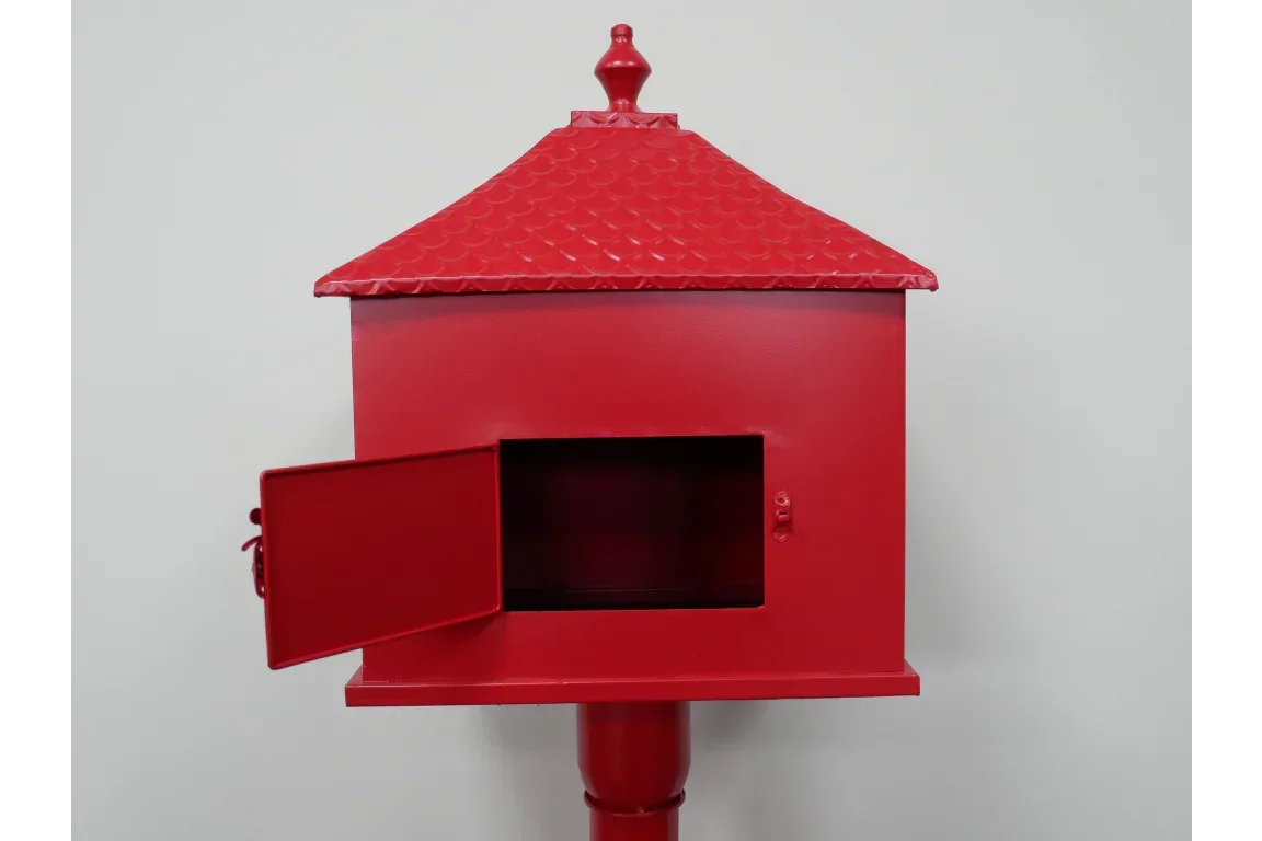 Red metal mailbox with open door and decorative roof, front view against plain wall