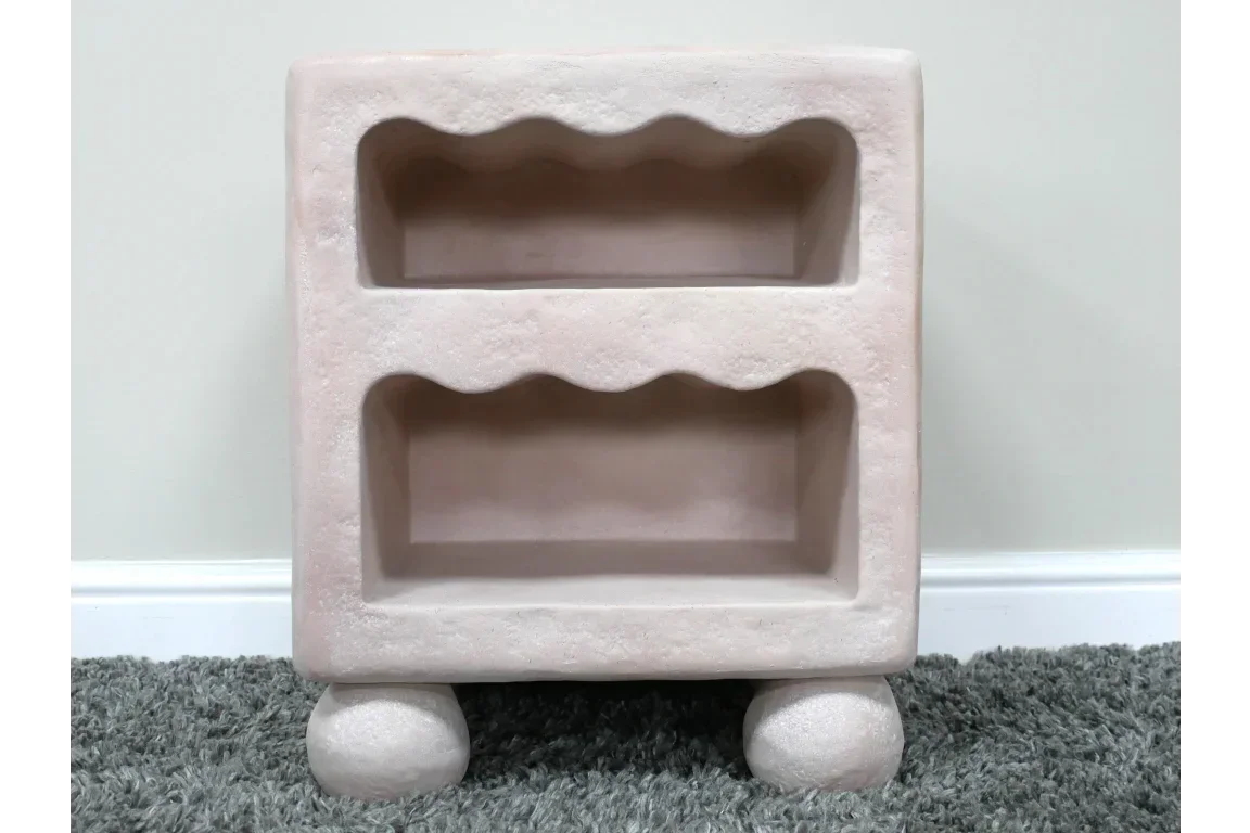 Beige concrete bedside table with two wavy-edge open shelves and round legs on carpet