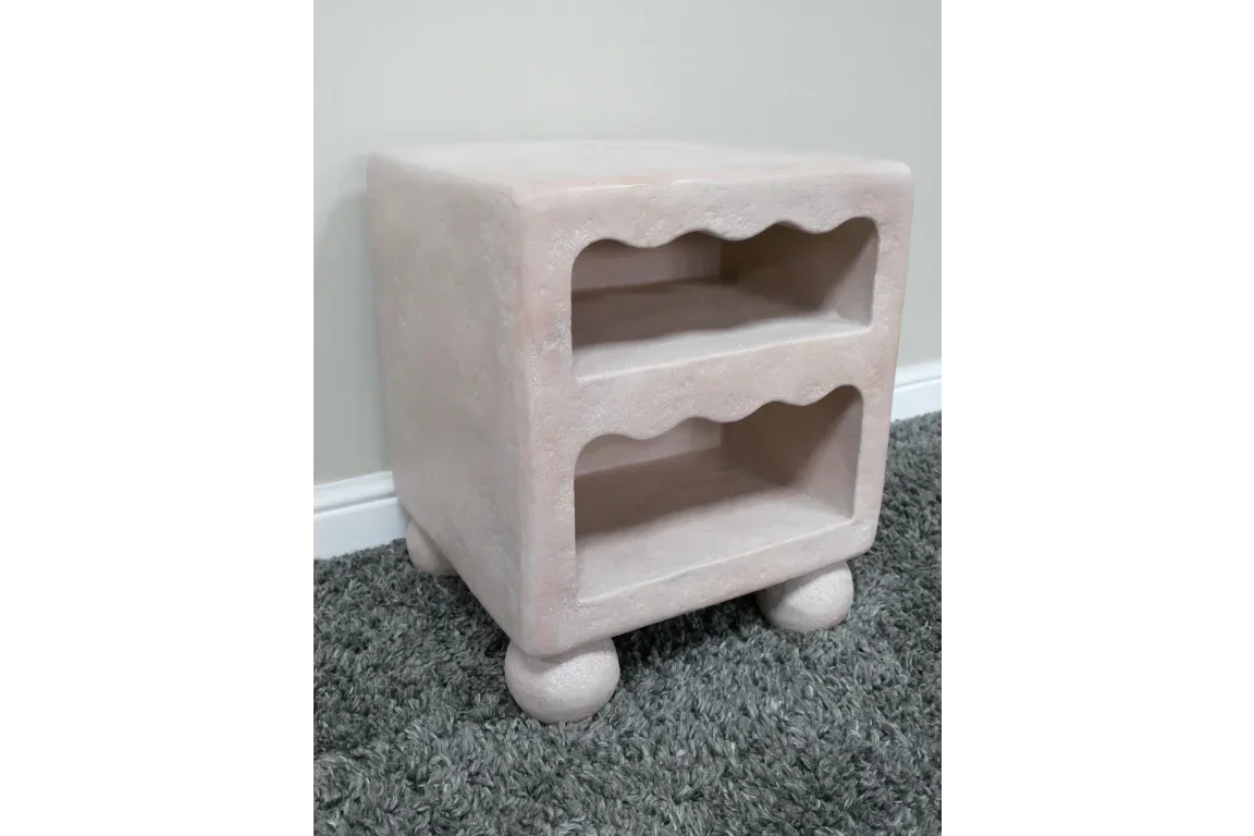 Beige bedside table with two open shelves and rounded legs on grey carpet