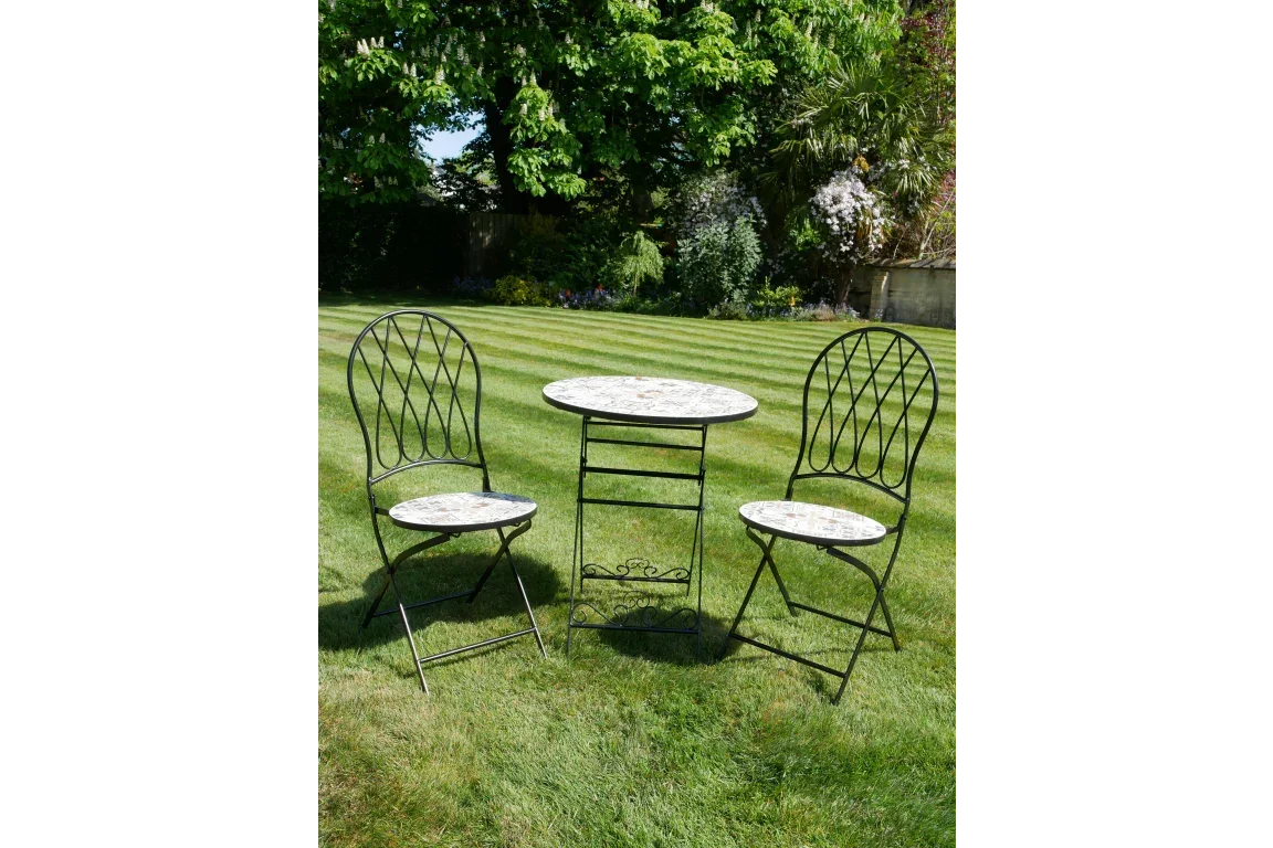 Mosaic garden bistro table and two metal chairs on lawn with greenery background