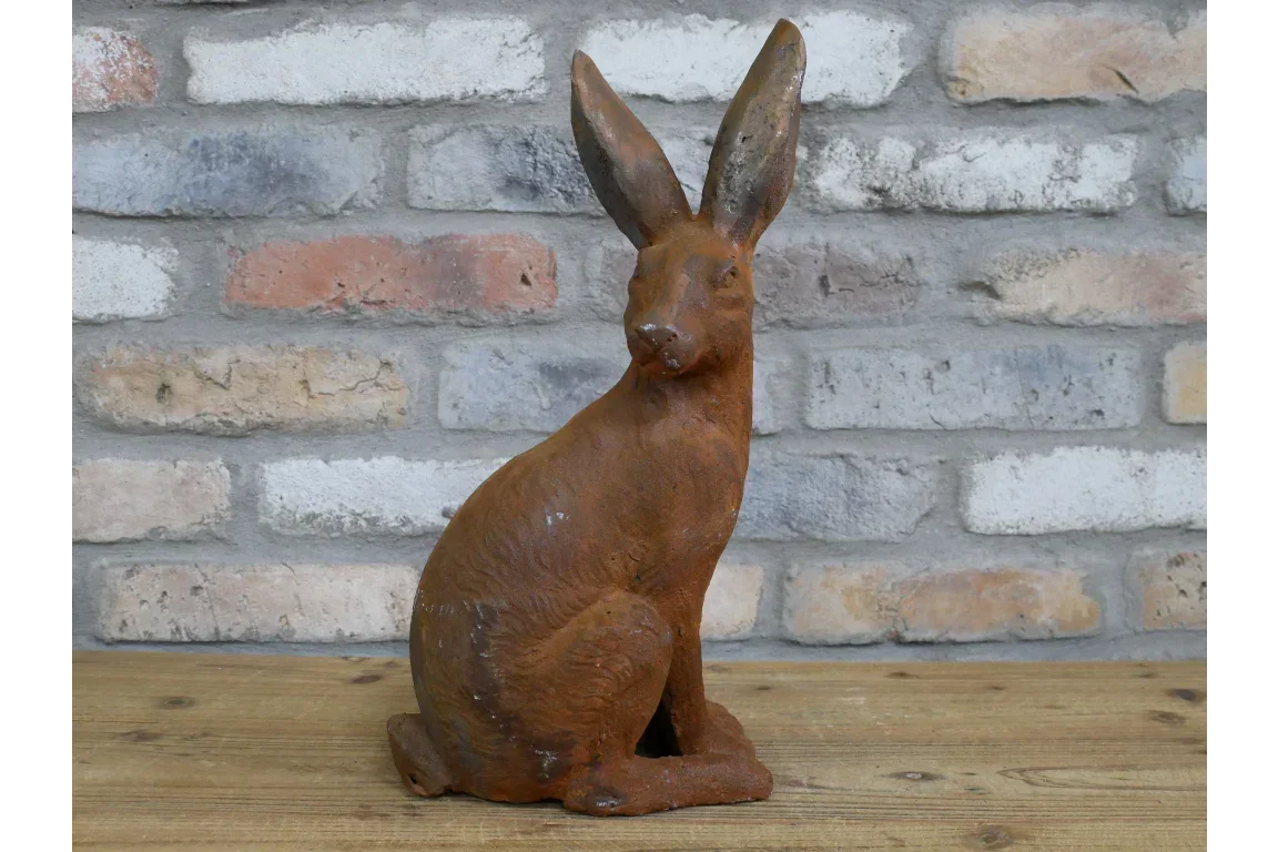 Cast iron rabbit ornament with rust finish on wooden surface against brick wall background