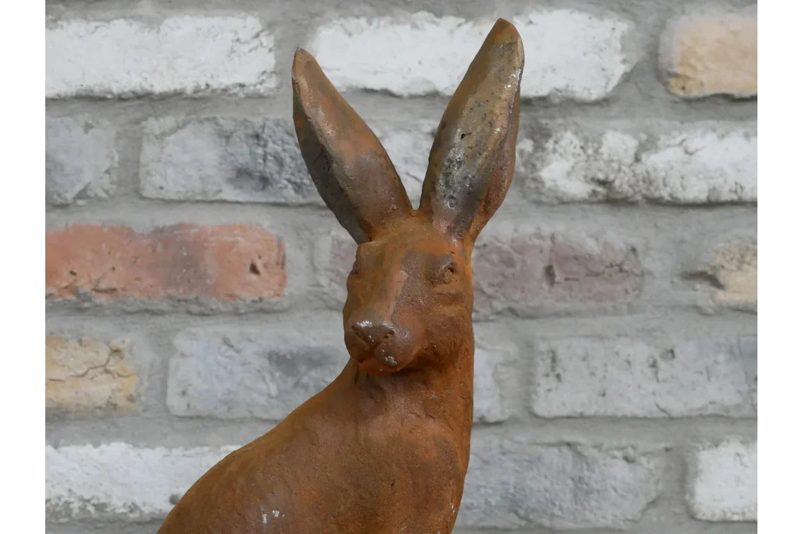 rust brown rabbit garden ornament with upright ears against rustic brick wall