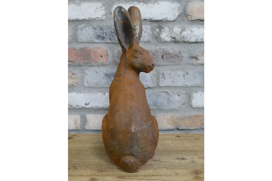 Rust effect rabbit garden ornament on wooden table with brick wall background