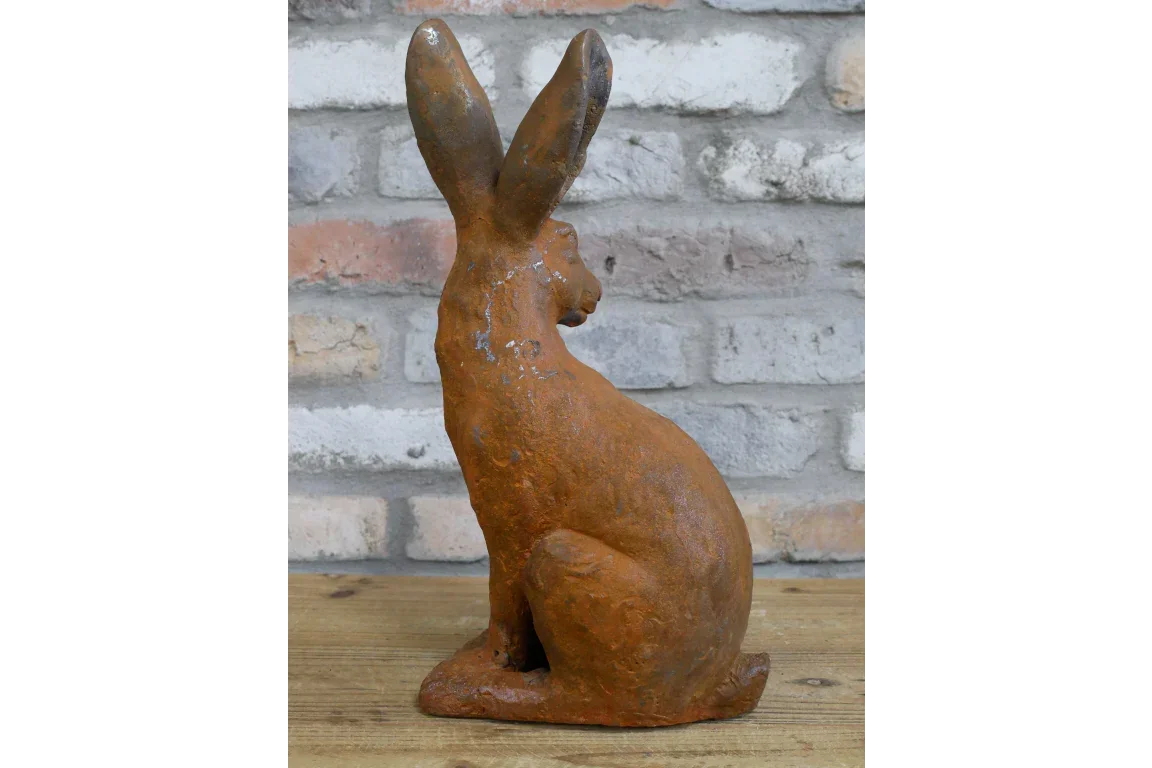 Cast iron hare ornament with rustic finish on wooden surface against brick wall backdrop