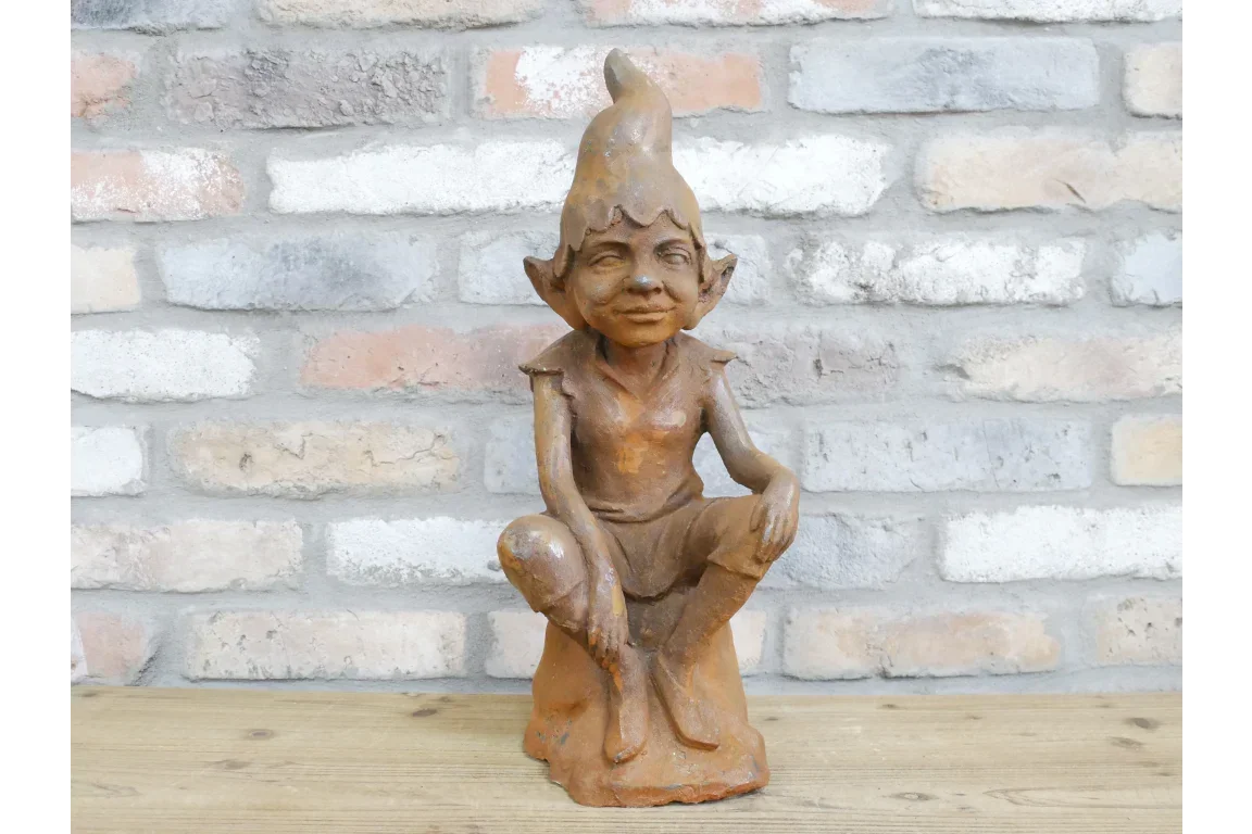 Rustic garden elf ornament seated on wooden surface with brick wall background