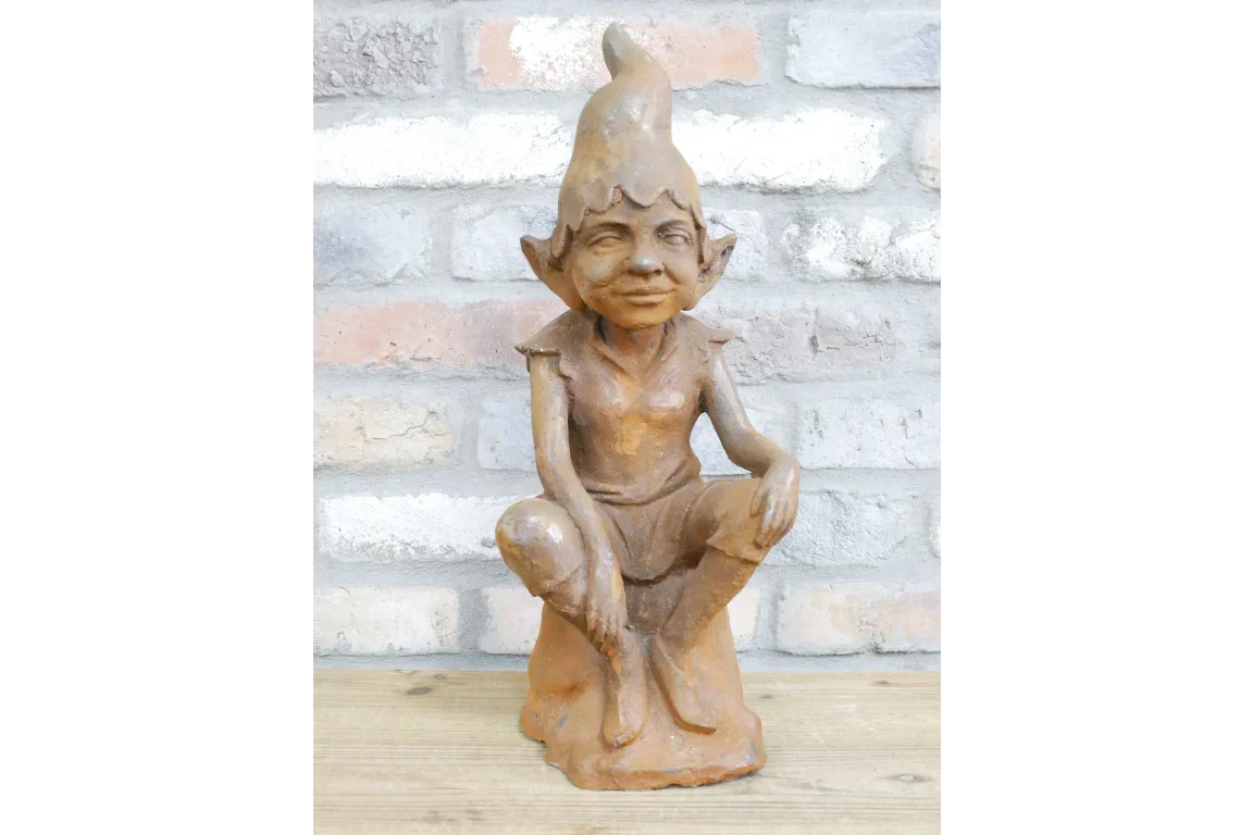 Rustic garden elf statue with pointed hat in seated pose on wooden surface