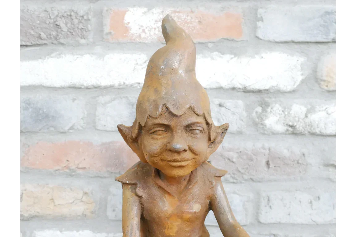 Rustic garden elf statue with pointed hat and ears against brick wall