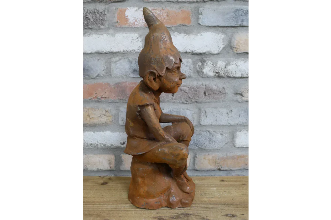 Rust finish garden gnome ornament seated on wooden table with brick wall background