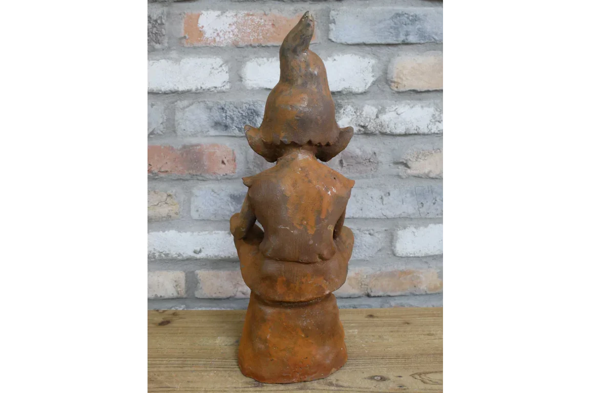 Rust effect garden ornament gnome figure facing brick wall, placed on wooden surface
