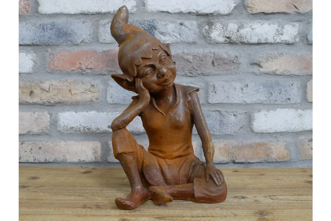 Rust effect resin garden elf ornament seated on wooden surface with brick wall background