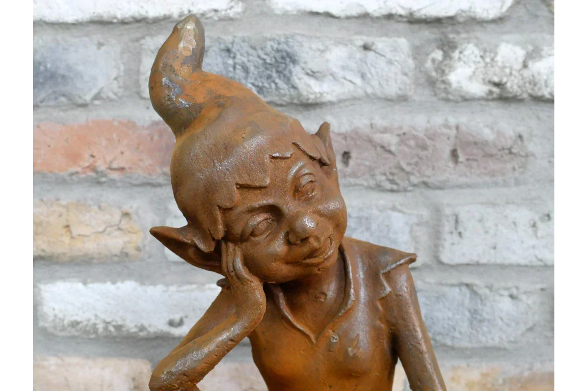 Rustic garden ornament of smiling elf leaning on hand, terracotta finish, brick wall background