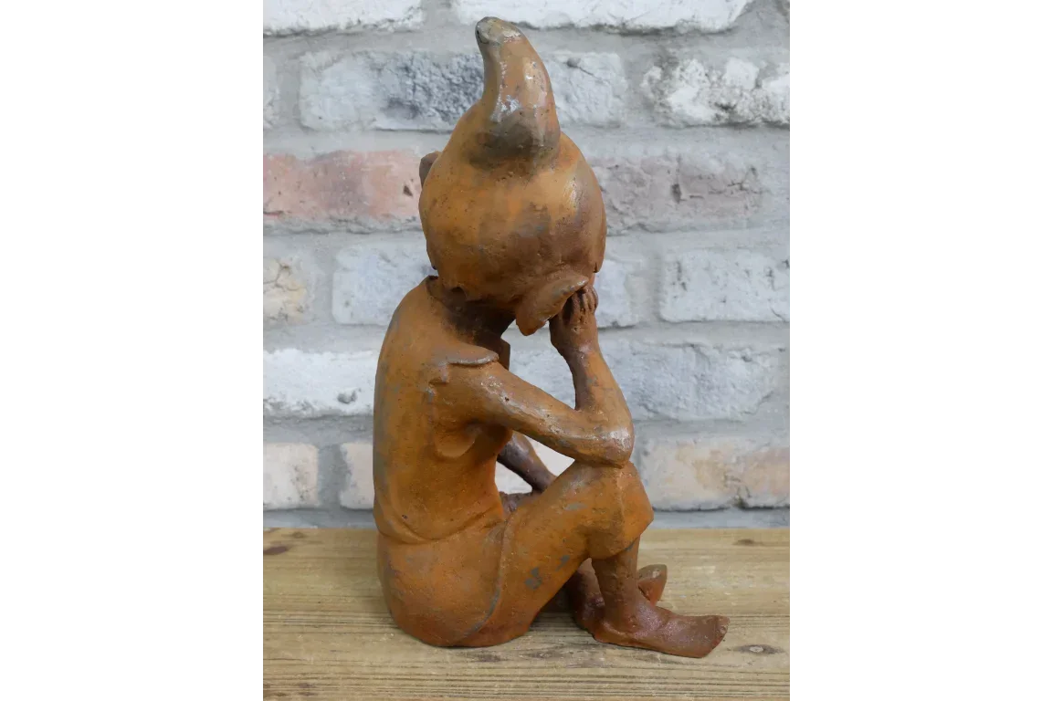 Rust effect garden ornament of seated figure with pointed hat on wooden surface