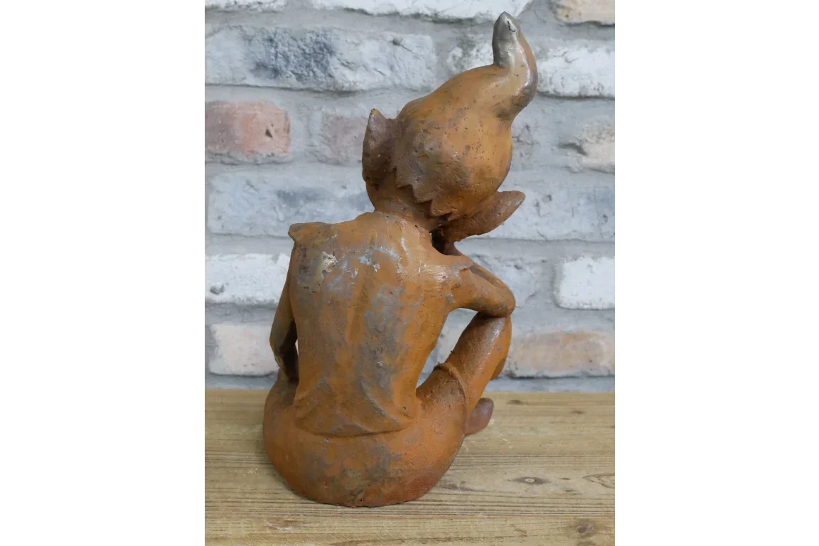 Rust garden ornament elf statue sitting on wooden surface with brick wall background