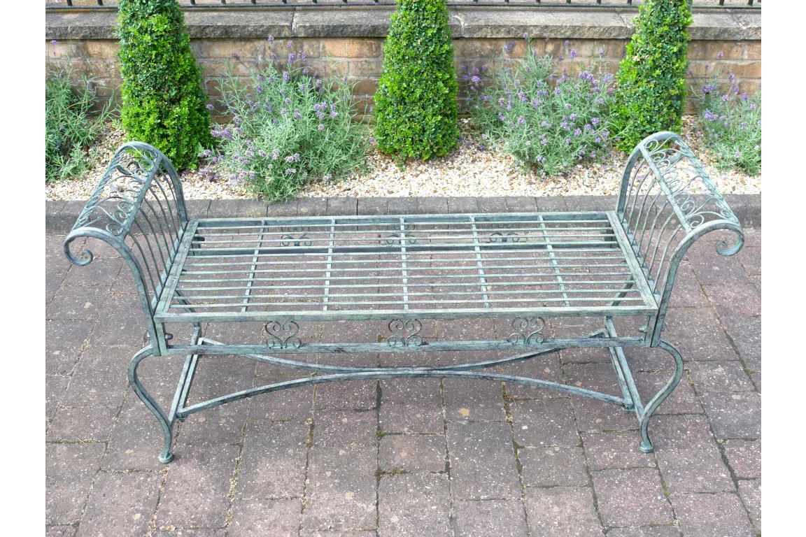 Metal garden bench with ornate scroll arms on patio in front of trimmed bushes
