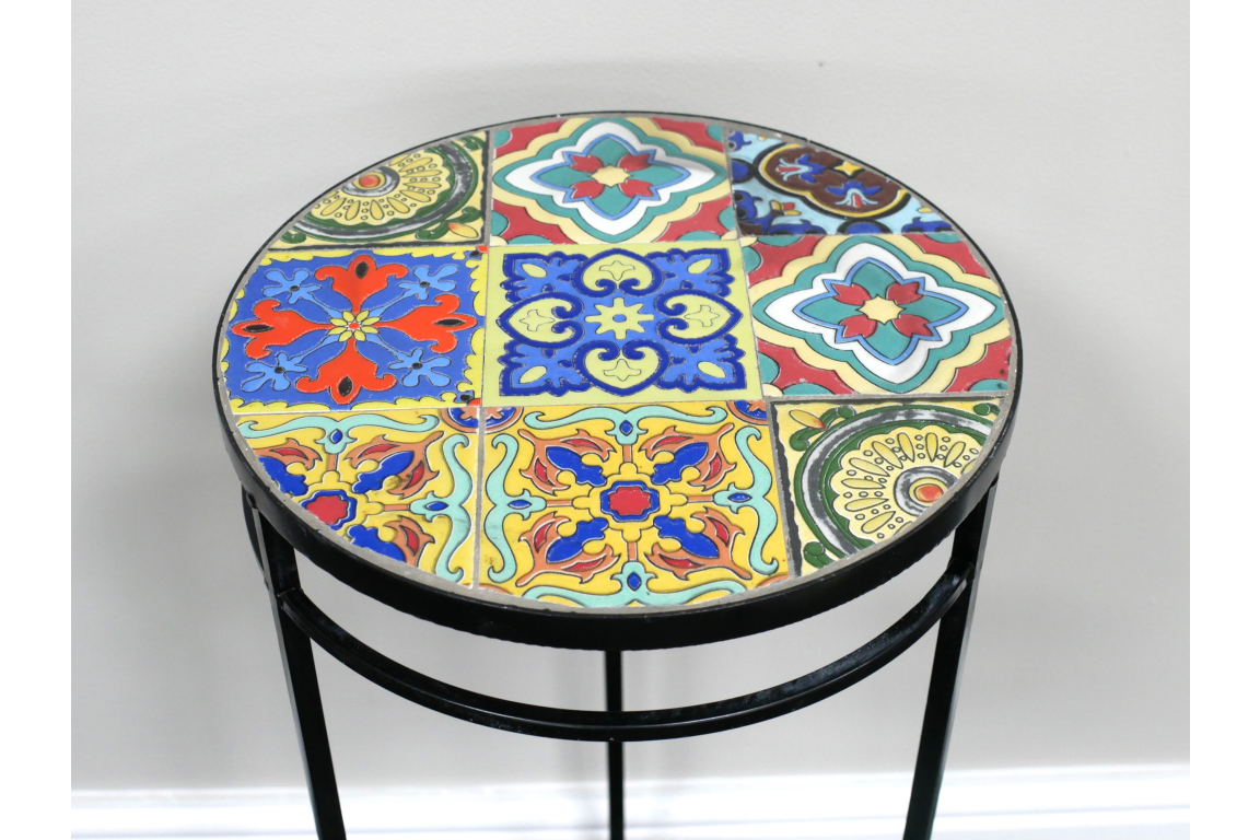 Round side table with multicolored patterned tile top and black metal frame, shown from an angled top view.