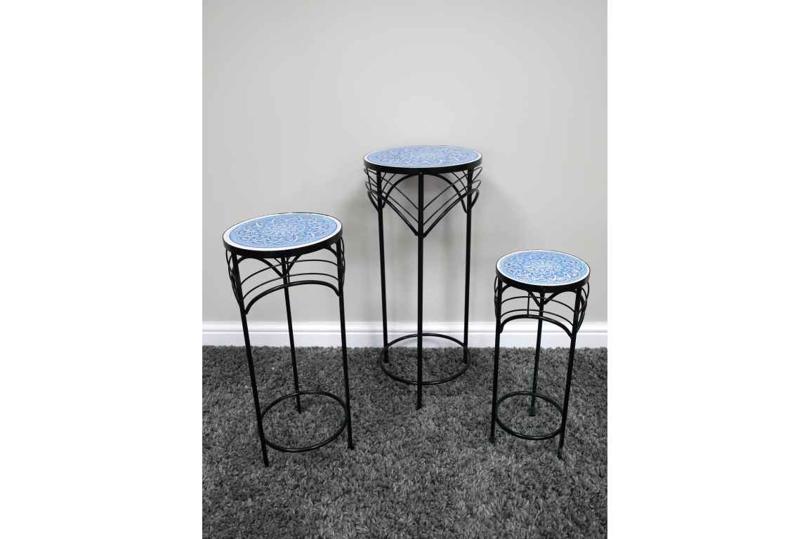 Set of 3 round side tables with black metal legs and blue patterned ceramic tops, shown on gray carpet against white wall.