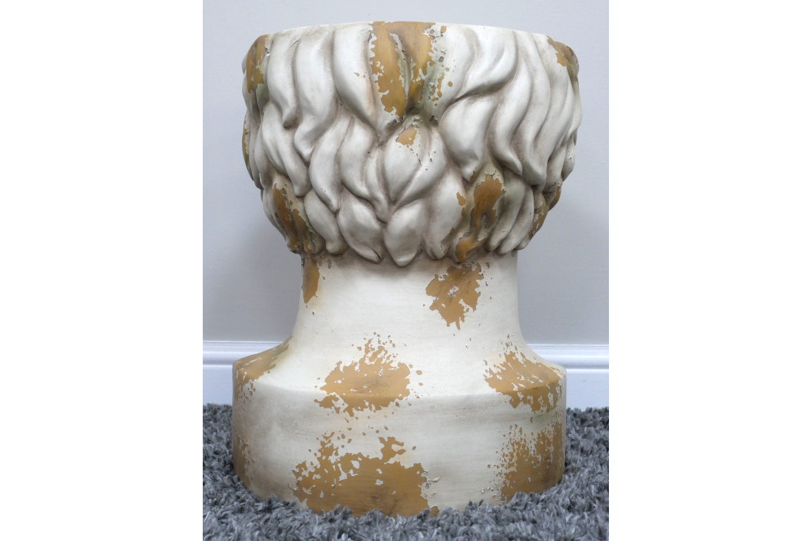 Round head-shaped side table in distressed white and gold finish, shown from rear on grey carpet.