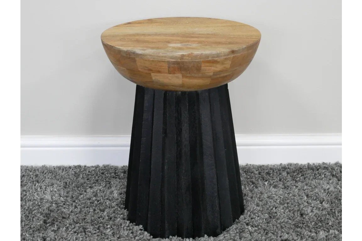 Round wooden side table with natural top and black fluted base on grey carpet