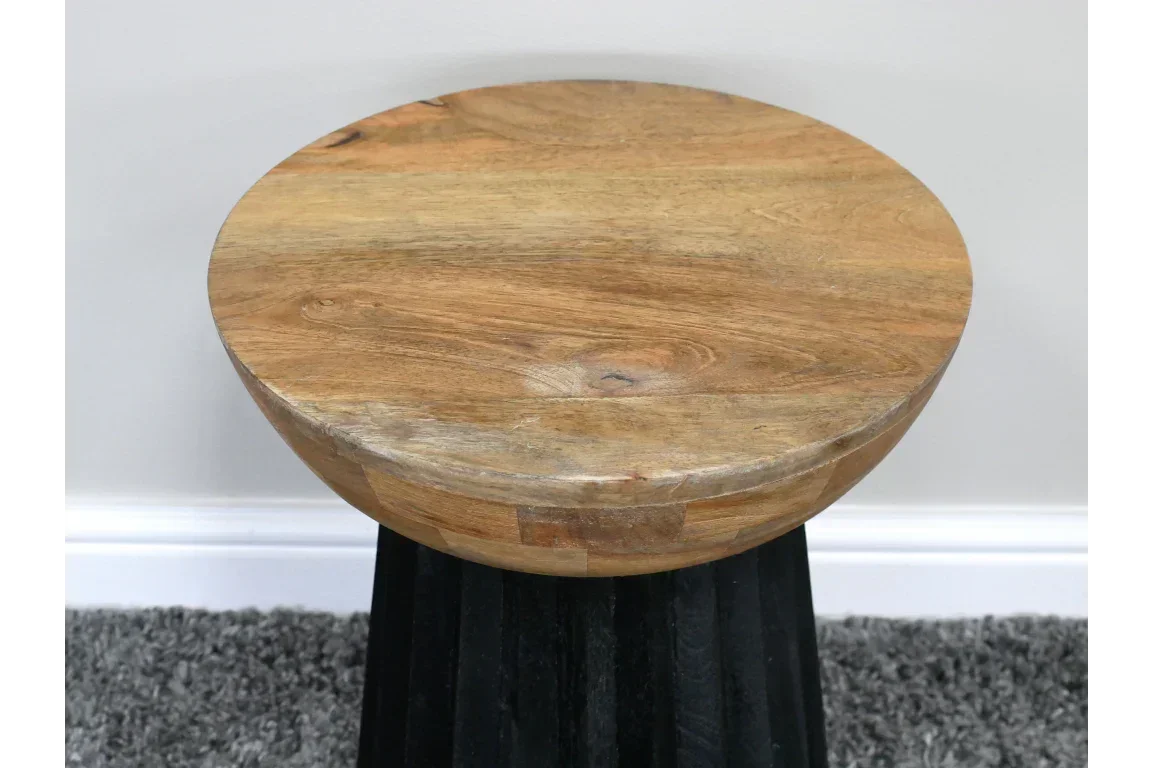Round solid wood side table with natural finish and black base on grey carpet