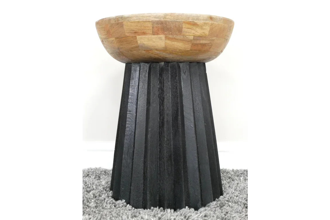 Round wooden side table with natural top and black angular base on grey carpet