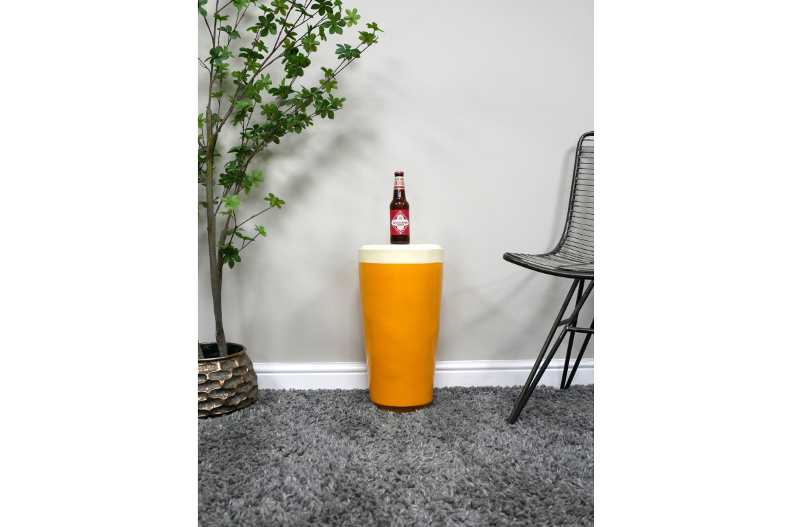 Cylindrical mustard yellow Lager Side Table with cream top, displayed on grey carpet between plant and black wire chair.