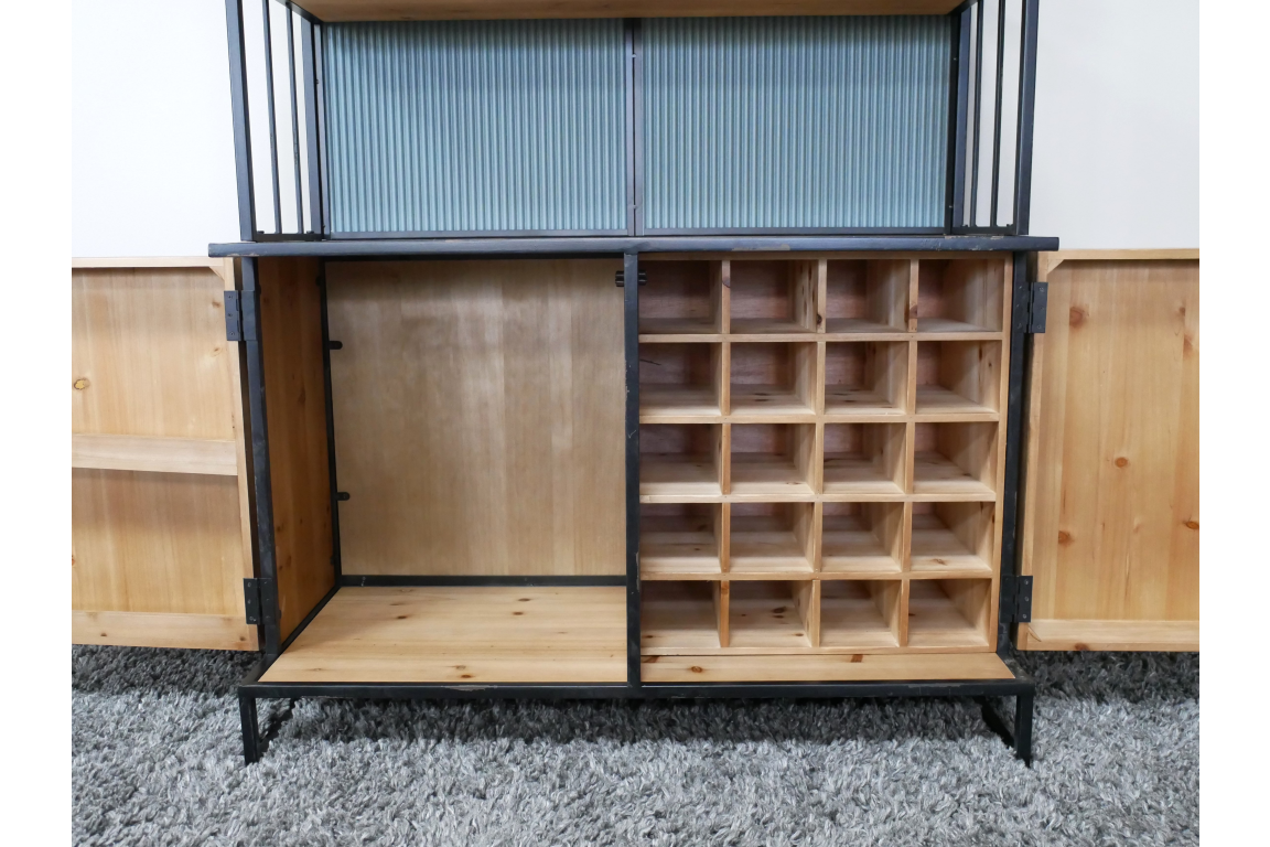 Wooden bar cabinet with black metal frame, open doors, divided bottle storage, and shelving on gray carpet.