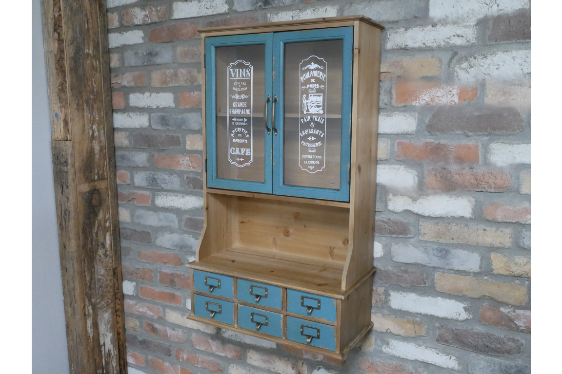 Wooden Parisienne wall unit with blue cabinet doors and six blue drawers, against a rustic brick wall, angled view.