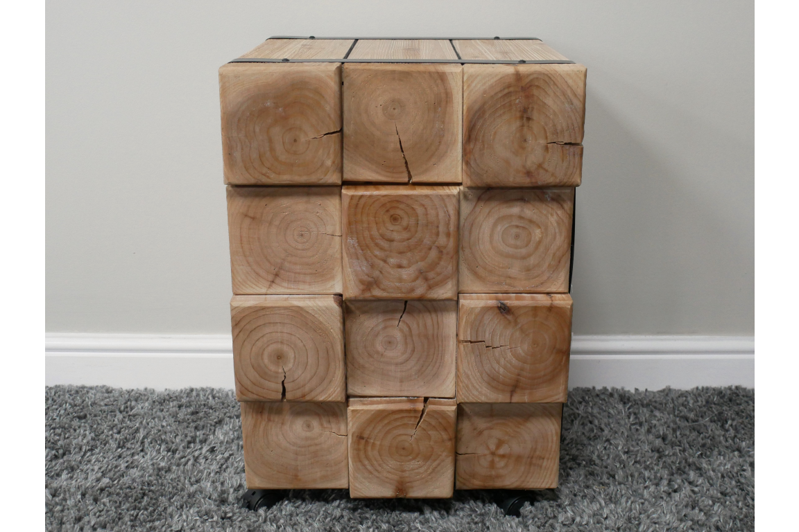 Chunky bedside cabinet made of natural wood blocks with visible grain and cracks, front view on carpeted floor.