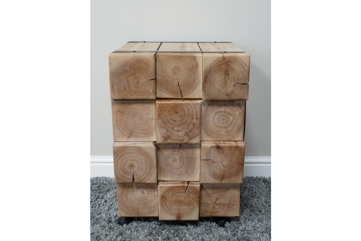 Chunky bedside cabinet made of natural wood blocks showing grain and cracks, front view on gray carpet.