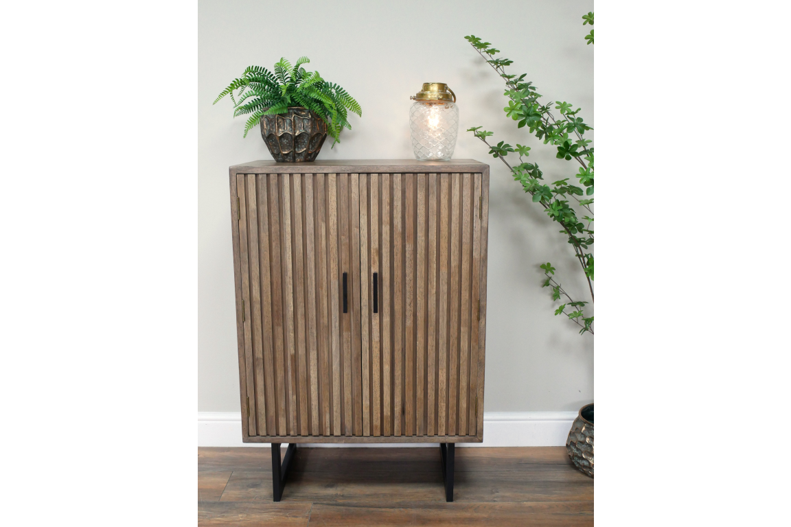 Wooden 2 door slatted cabinet in natural finish with black handles and legs, shown from front in indoor setting.
