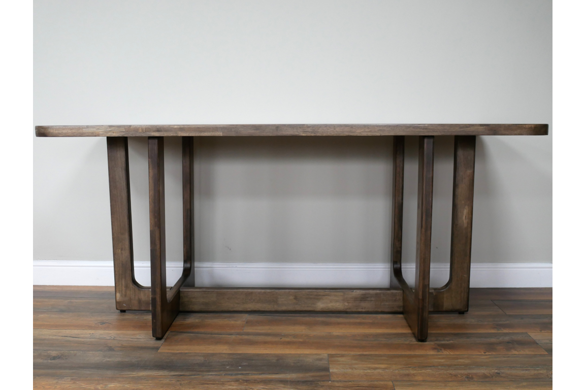 Rectangular dining table with dark wooden top and sturdy legs, shown from the front against a plain wall.