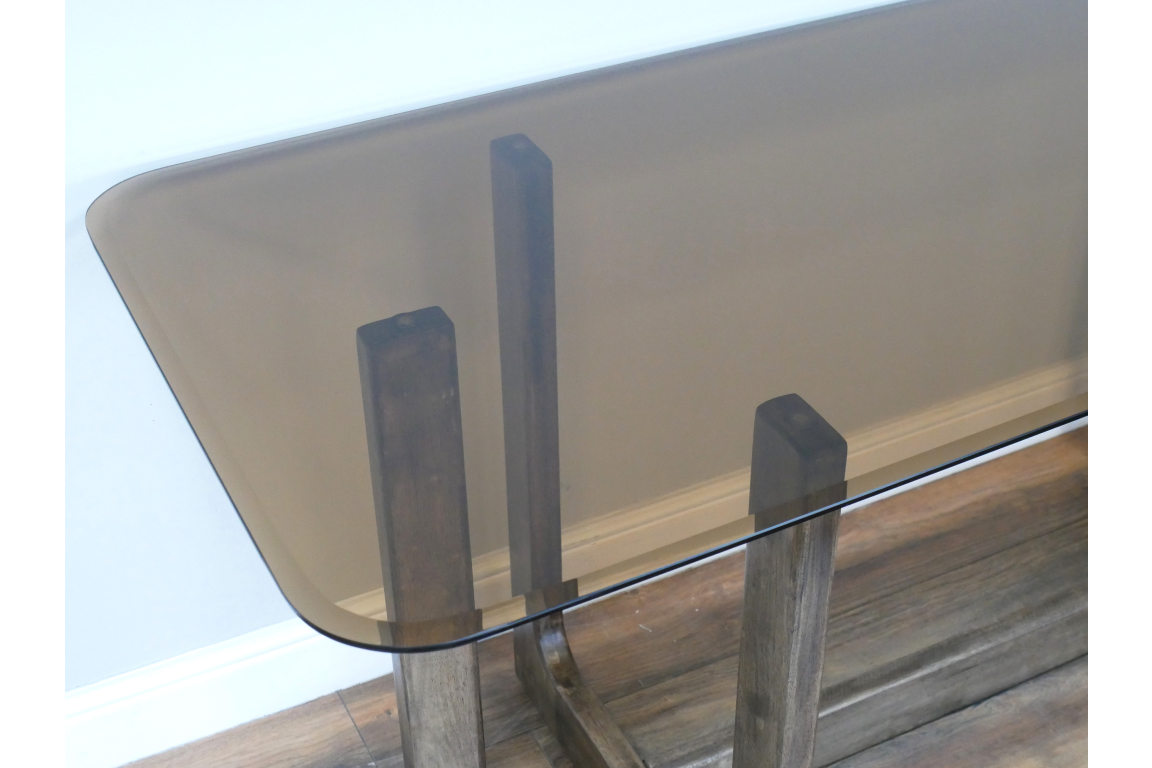 Rectangular dining table with tinted glass top and wooden legs, shown from a top corner angle.