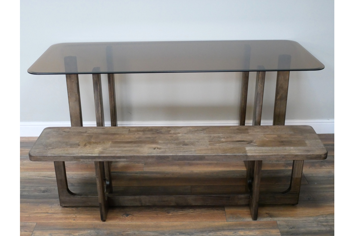 Rectangular dining table with smoky glass top and rustic brown wooden base, shown front view on wooden floor.