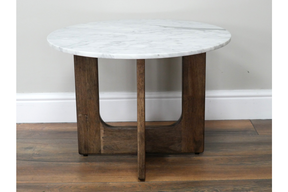 Round marble top side table with dark wooden legs, shown from front on hardwood floor against white wall.