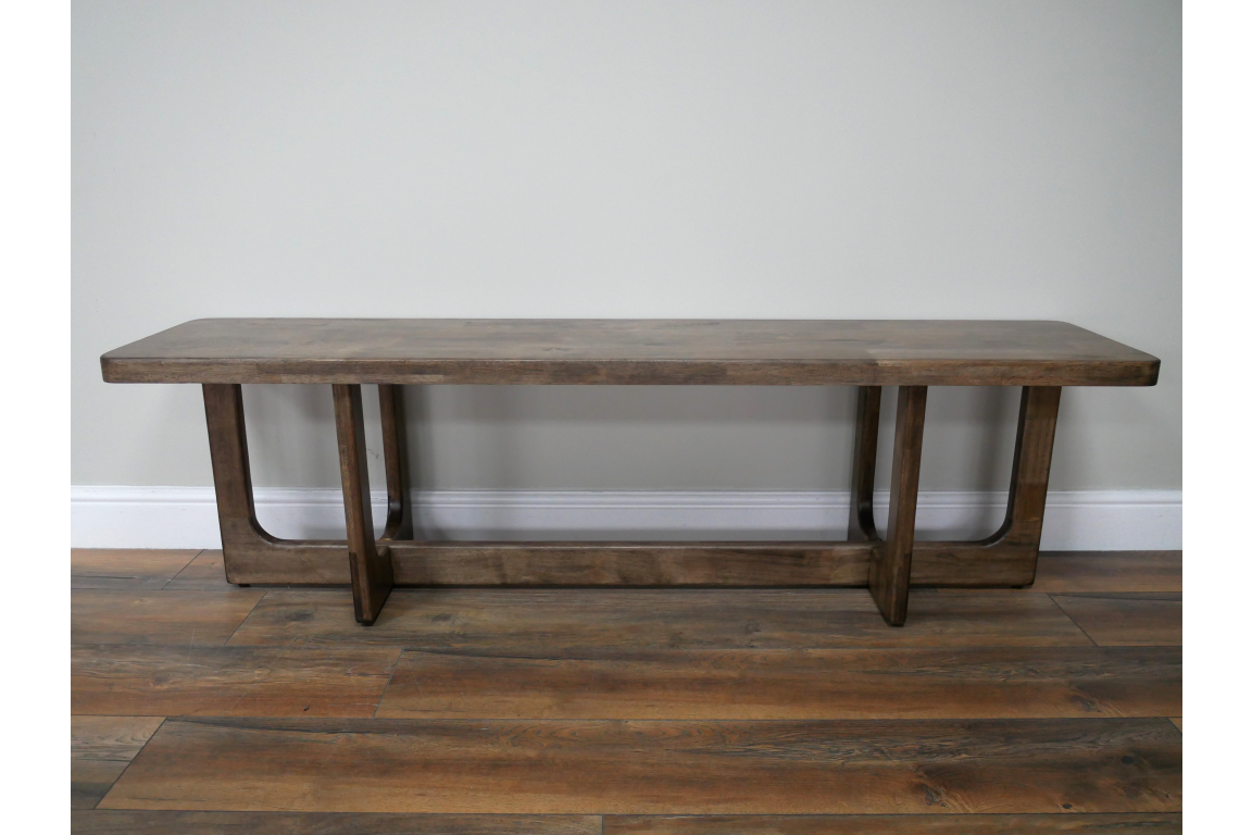 Long wooden bench with a rectangular top and U-shaped legs, shown from the front on wooden flooring.