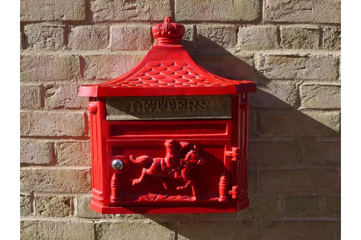 Red cast iron wall-mounted post box with horse design on brick wall