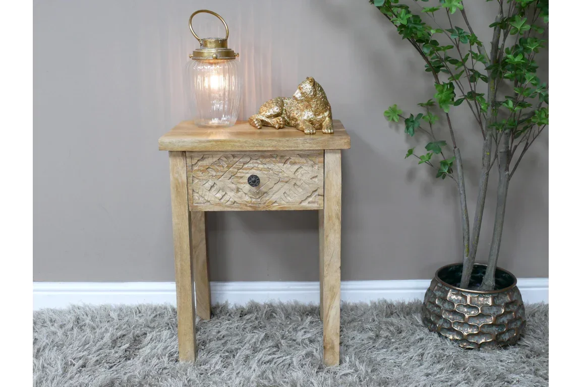 Natural wood bedside table with carved drawer, lamp, and gold ornament on top