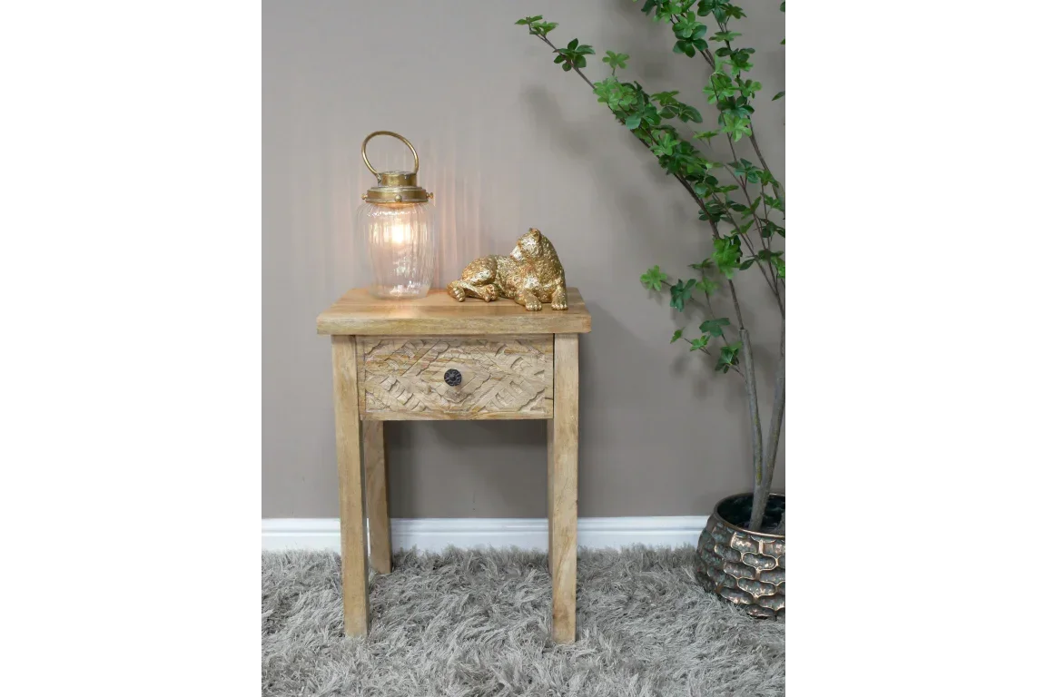 Wooden bedside table with carved drawer, lantern, gold ornament, and indoor plant