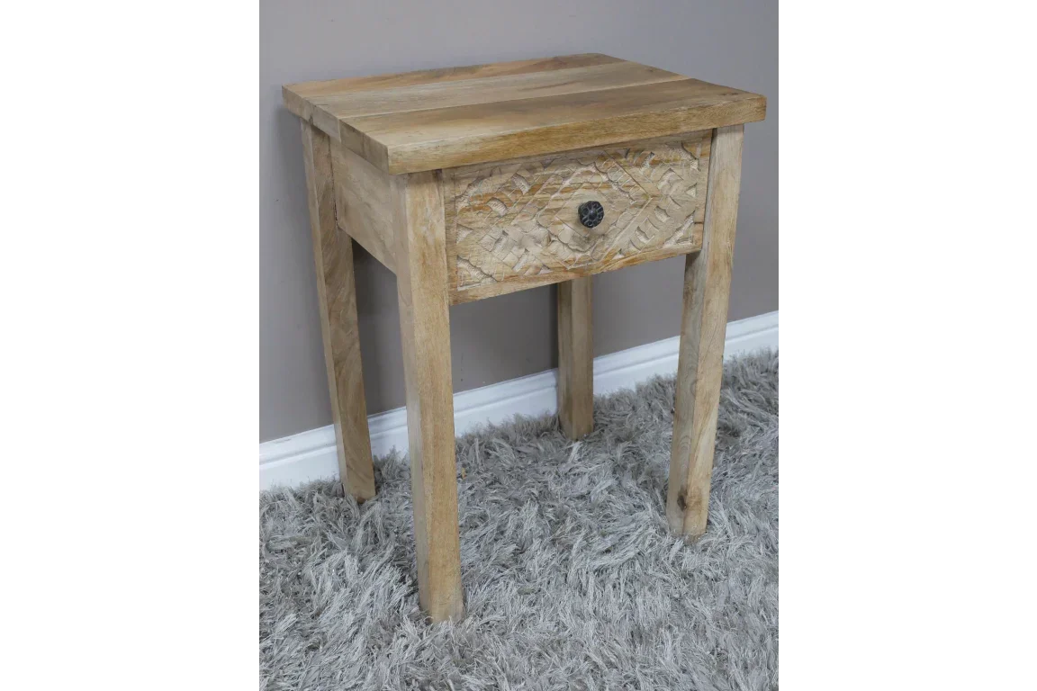 Light wood bedside table with single drawer and carved front detail on grey rug