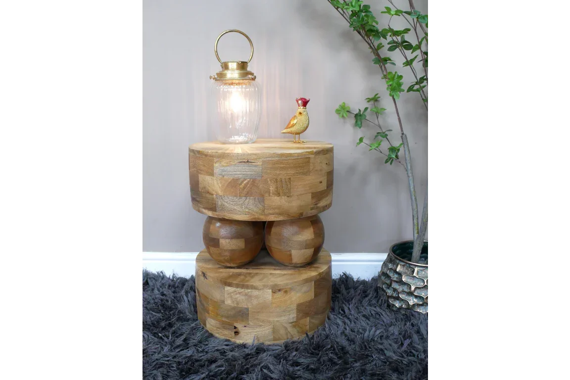 solid wood side table with round base displayed on grey rug with lamp and plant