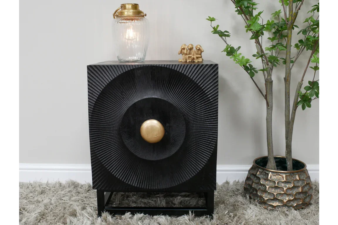 Black wooden side table with textured front and gold knob, styled with decor and plant