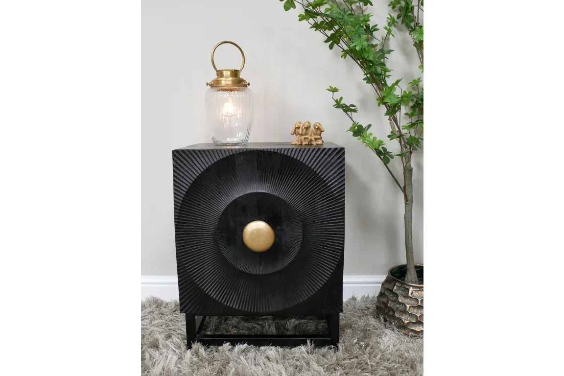 Black wooden cabinet with textured circular front and gold handle, styled with lantern