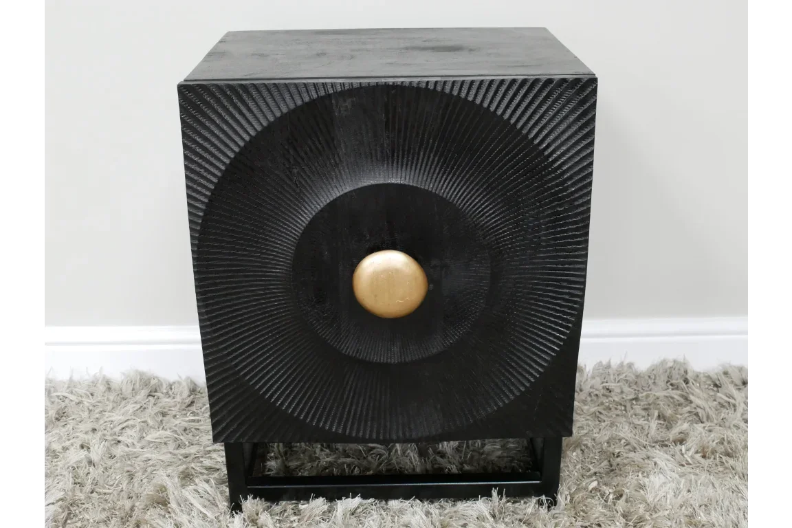 Black wooden side table with textured front and gold circular handle on plush rug