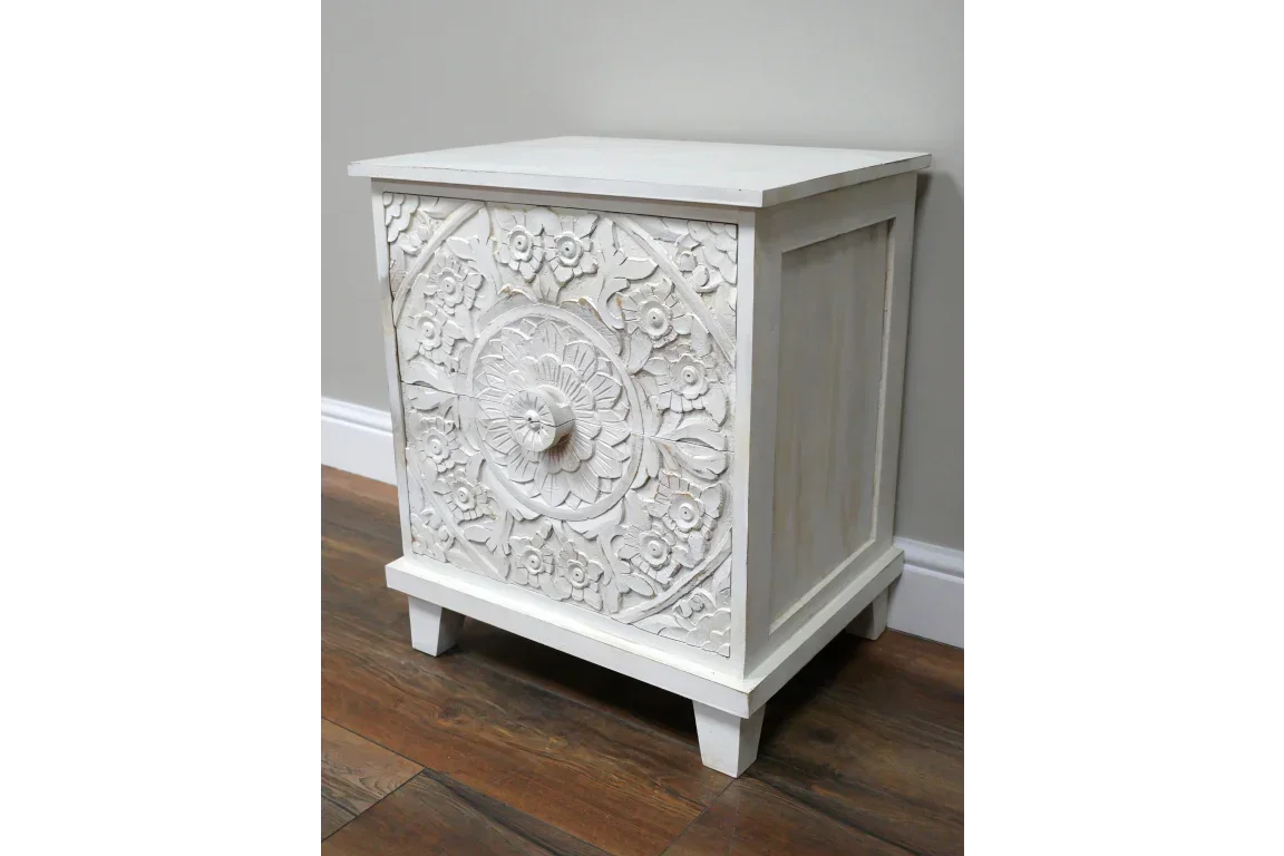 White wooden nightstand with carved floral detail on front panel, side view on wood floor