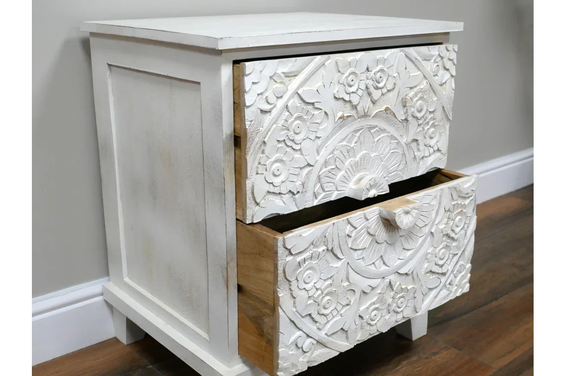 White carved wooden bedside table with floral pattern and two open drawers on wood floor